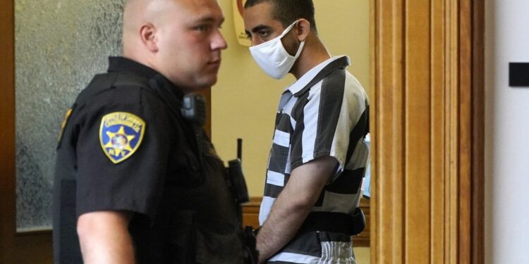 Hadi Matar, 24, background, leaves an arraignment in the Chautauqua County Courthouse in Mayville, NY., Saturday, Aug. 13, 2022. Matar, accused of carrying out a stabbing attack against “Satanic Verses” author Salman Rushdie, has entered a not-guilty plea on charges of attempted murder and assault. (AP Photo/Gene J. Puskar)